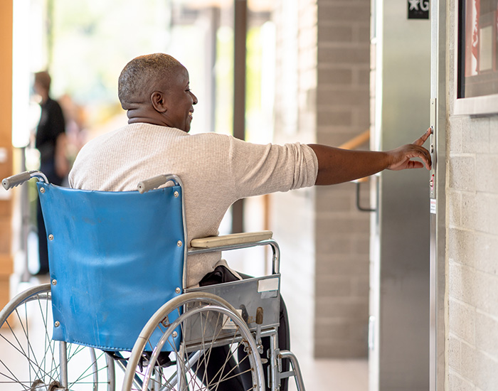 Person in a wheelchair pressing an elevator button loading=