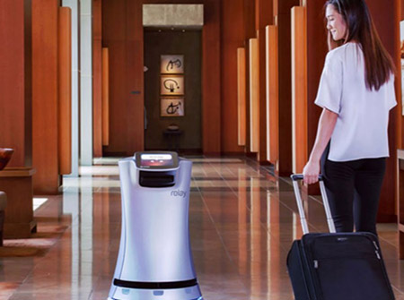 Woman with rolling suitcase in hotel lobby walking with service robot 