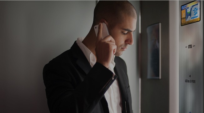 Man on the phone in an Otis lift.  There is also an eView screen in the control panel of the lift for a modern lift car interior design