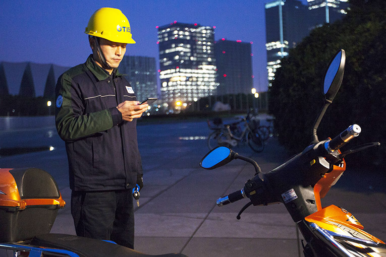 Otis employee looking at the app on a phone in behind a motorcycle in front of building