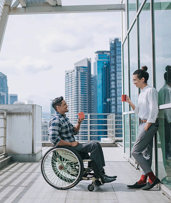 Man in a wheelchair having coffee with a colleague on a building roof patio