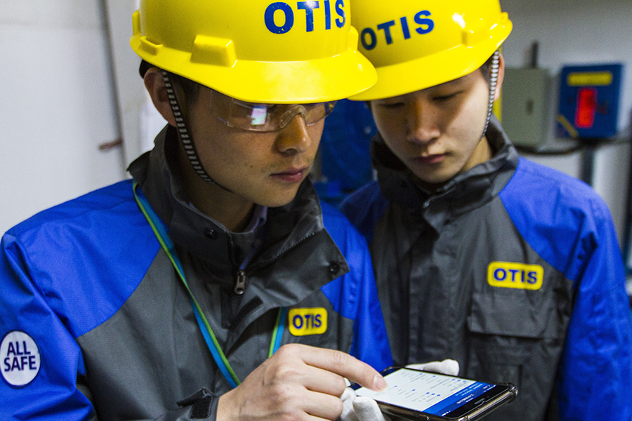 Two Otis employees looking at the Otis ONE tool on a mobile device