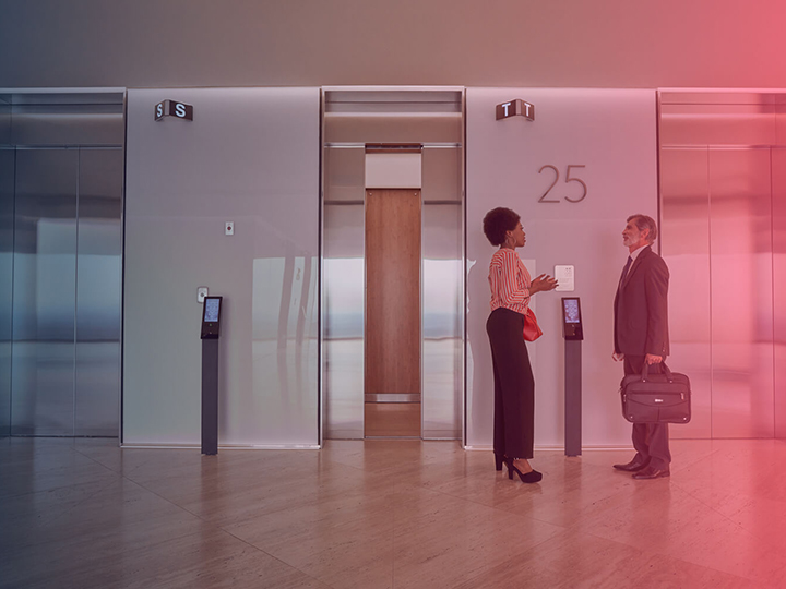 Business woman and business man standing in front of an elevator bank loading=