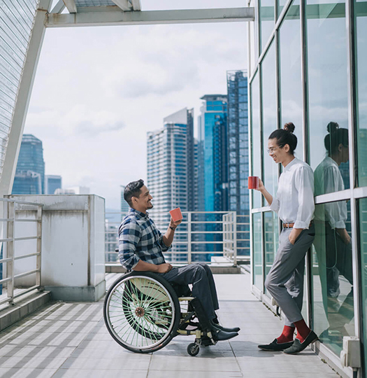 Man in a wheelchair having coffee with a colleague on a building roof patio