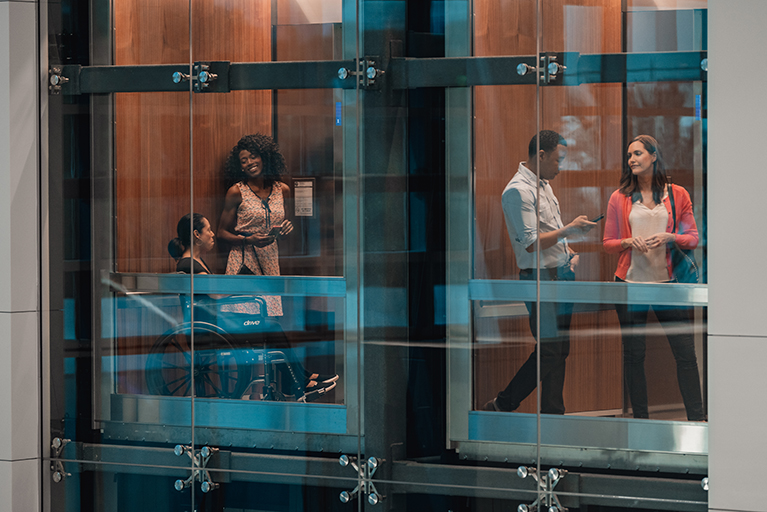 Side by side glass elevators with people on them 