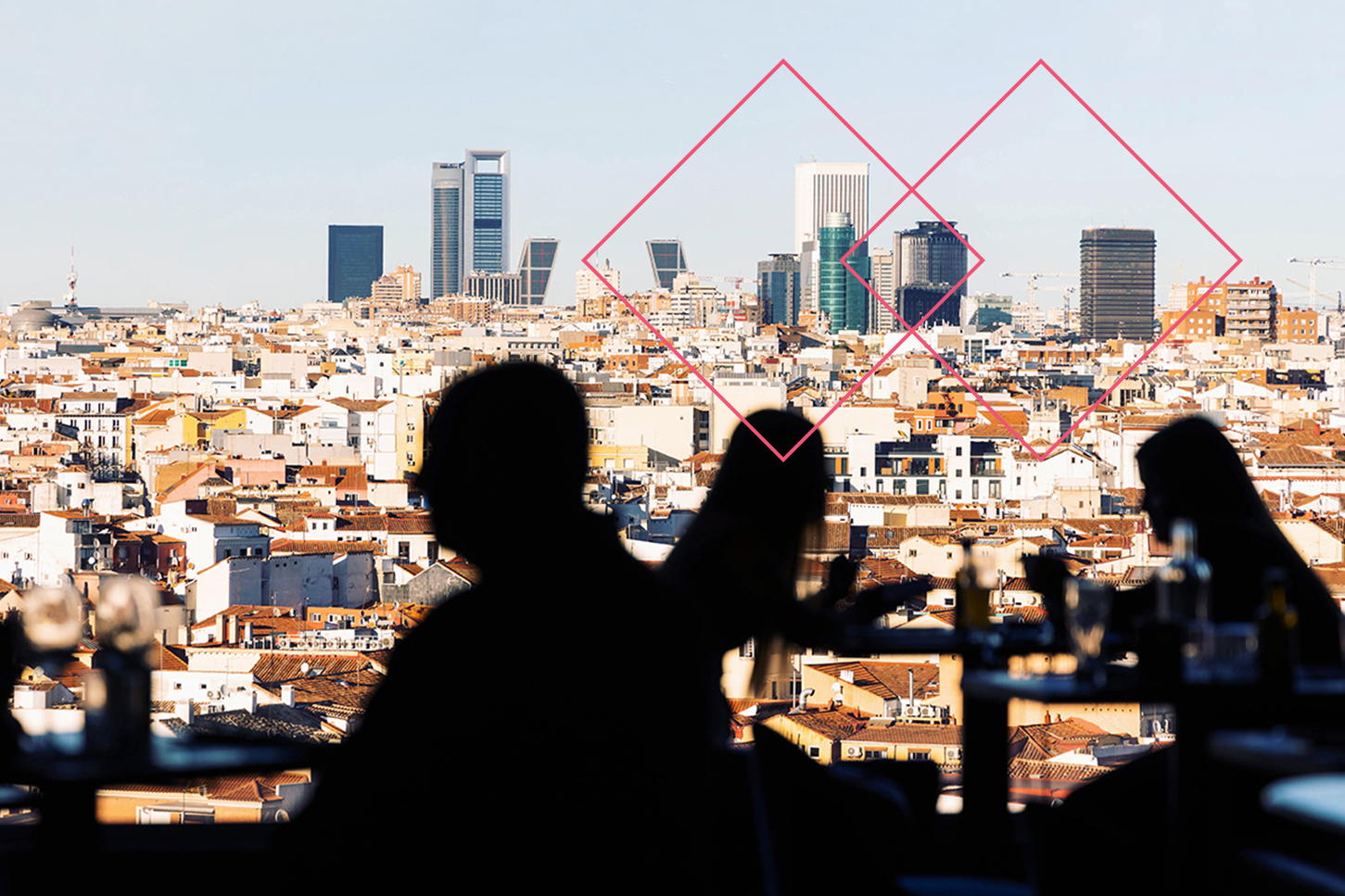 Silhouettes of people sitting down at tables, with city skyline in the background.