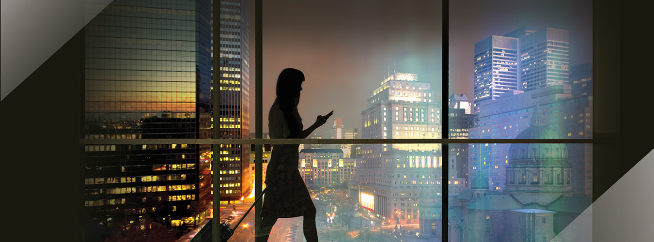 Silhouette of a woman standing by a window looking out over a city landscape.