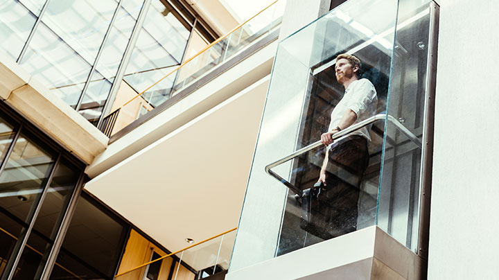 man-looking-out-glass-elevator_720x404